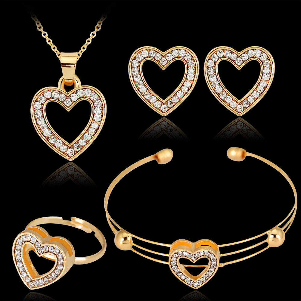Gold heart-shaped jewelry set including necklace, earrings, ring, and bracelet on a black background.