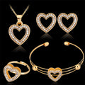 Gold heart-shaped jewelry set including necklace, earrings, ring, and bracelet on a black background.