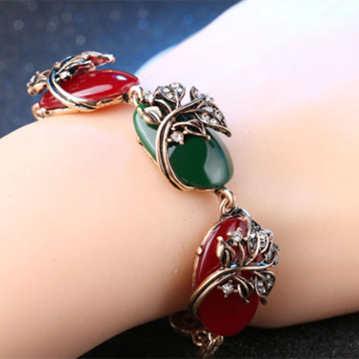 Bracelet with red and green stones on a wrist against a dark background