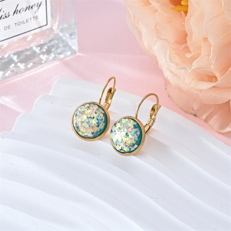 Gold earrings with green gemstones on a white card with pink flowers in the background