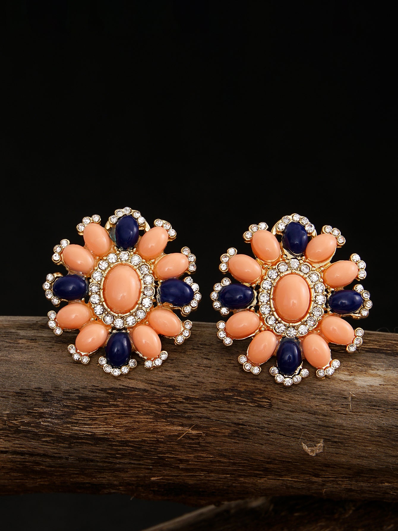 Pair of floral earrings with orange and blue stones on a dark background