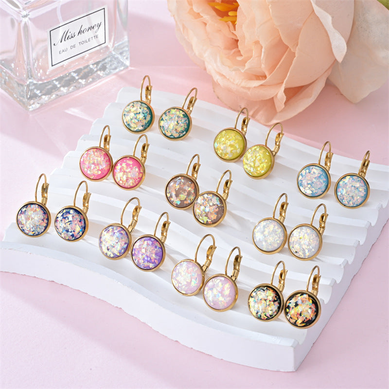 Set of colorful earrings on a display card with a perfume bottle and flowers in the background.