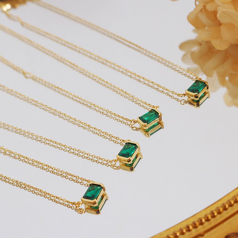Gold necklaces with emerald green pendants on a white surface.