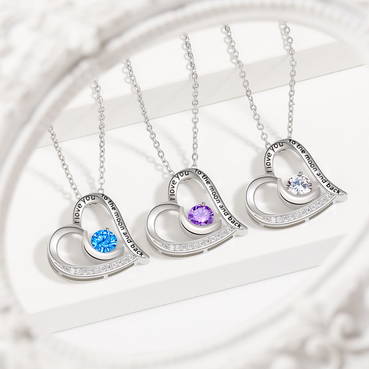 Three silver heart-shaped necklaces with embedded gemstones on a white background