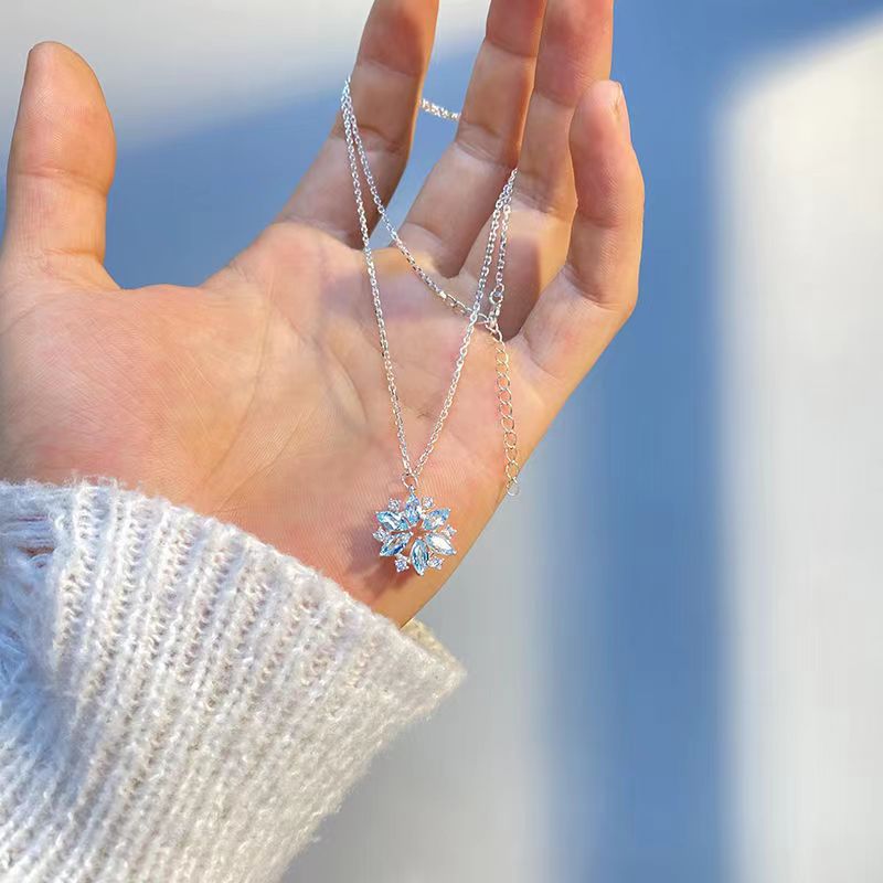 Hand holding a silver necklace with a snowflake pendant against a blurred outdoor background