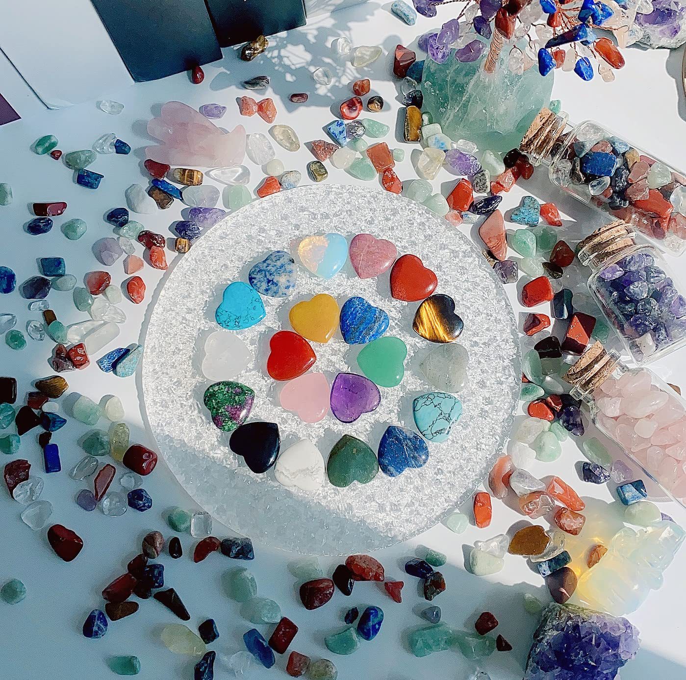 Colorful heart-shaped stones arranged in a circular pattern on a white surface with additional stones scattered around.