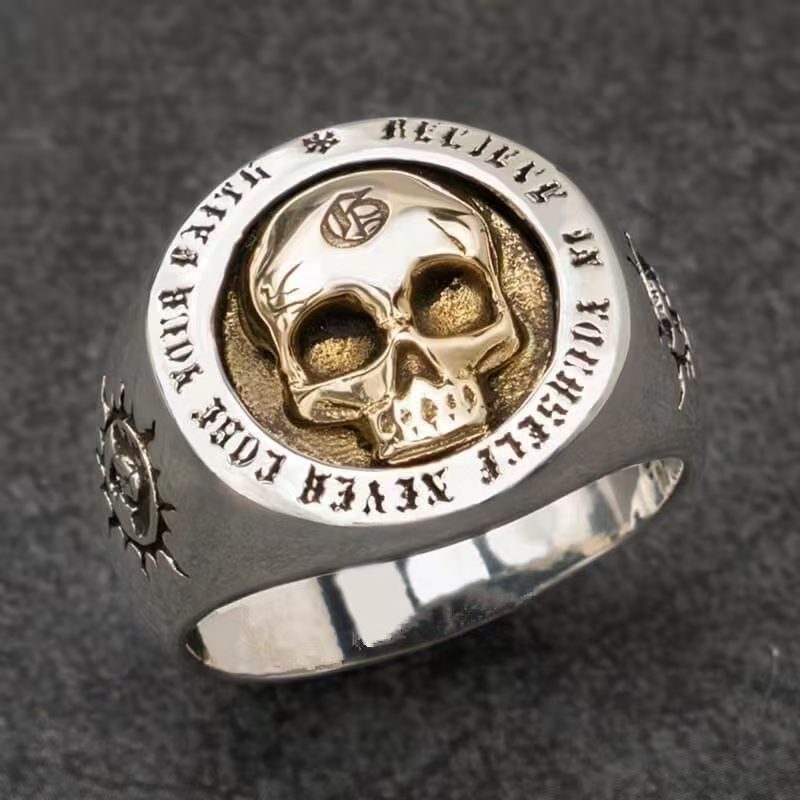 Silver ring with gold skull design and engraved text on a dark background