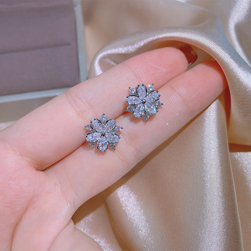 Flower-shaped earrings held between fingers against a satin background