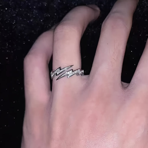 Hand wearing a silver ring with a lightning bolt design on a black background