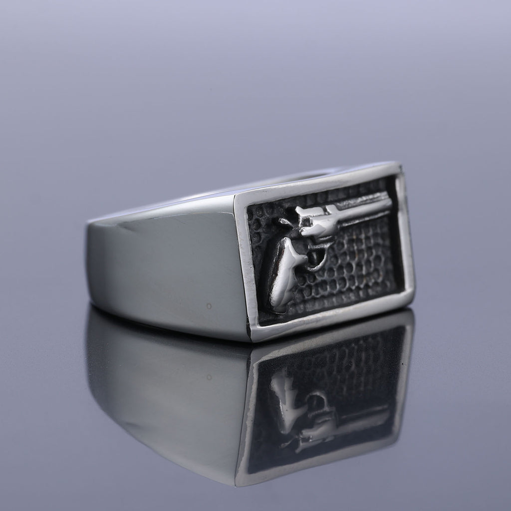 Silver ring with a gun emblem on a reflective surface