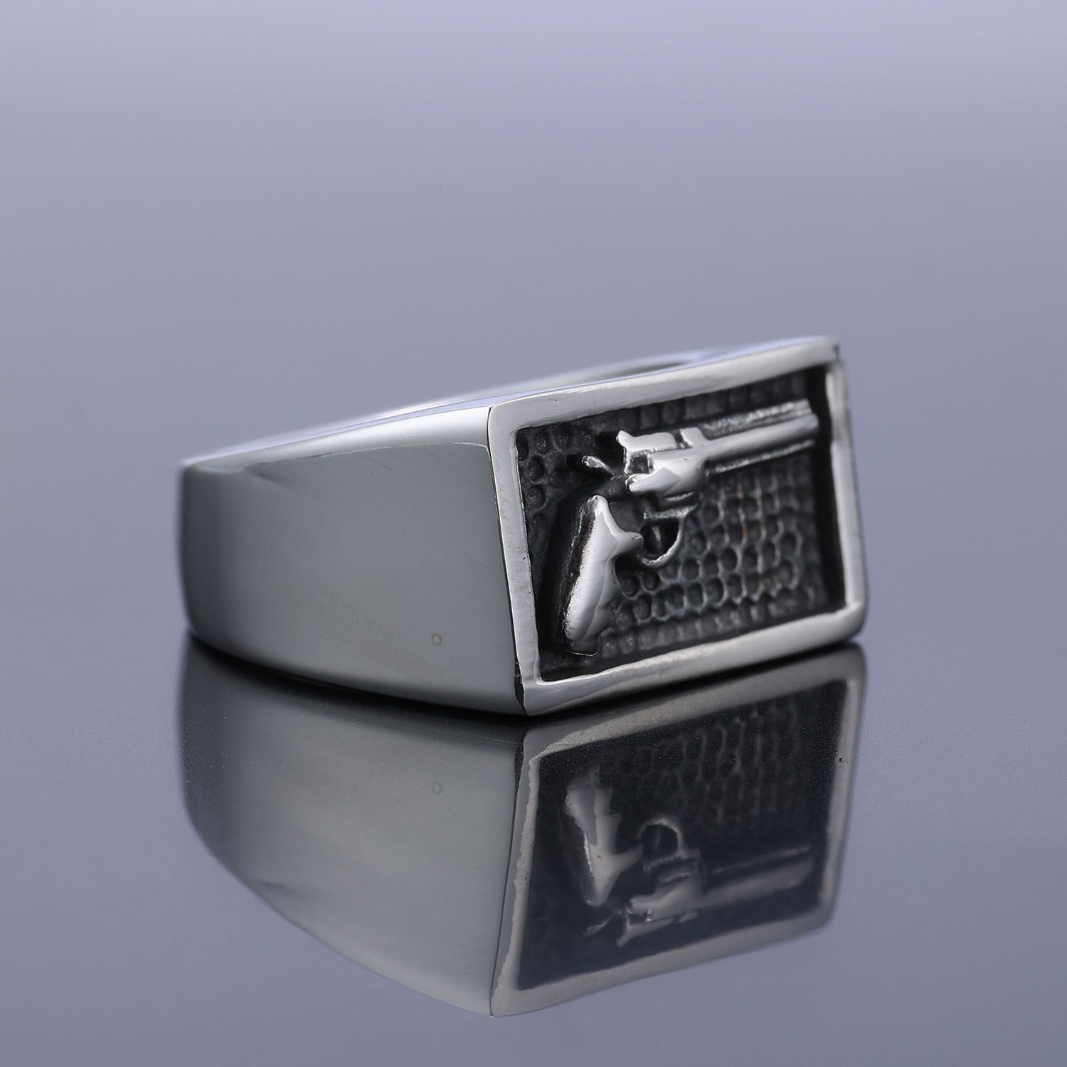 Silver ring with a gun emblem on a reflective surface