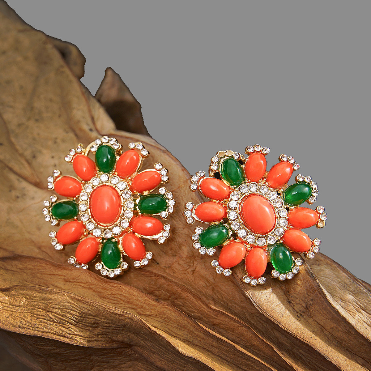Pair of floral earrings with orange and green stones on a wooden surface