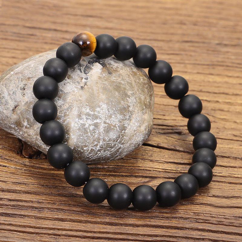 Black beaded bracelet with a wooden bead on a stone and wooden surface