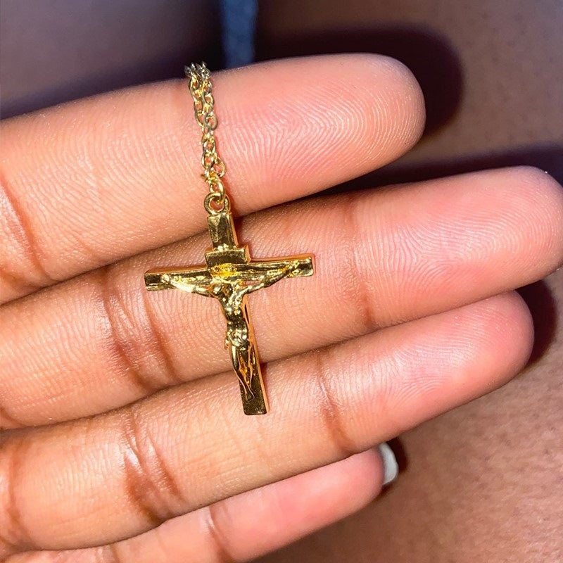 Gold crucifix pendant on a chain held between fingers