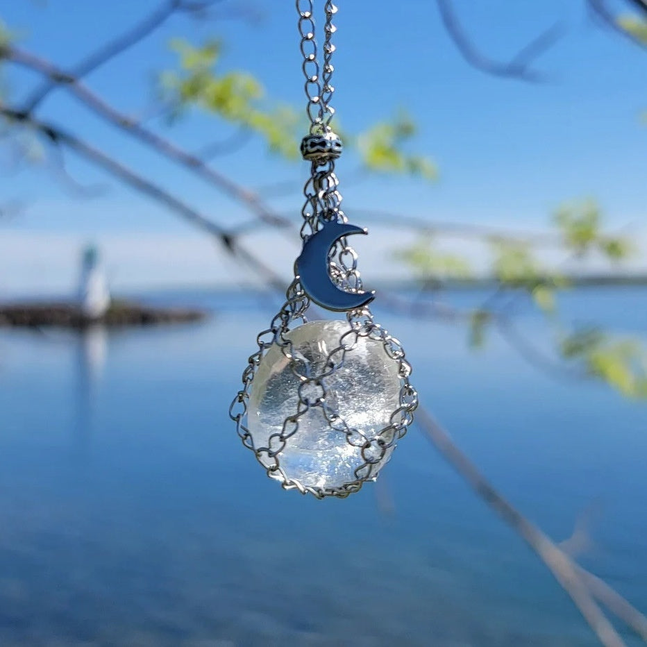 Necklace with a clear stone pendant and blue moon charm against a blurred natural background