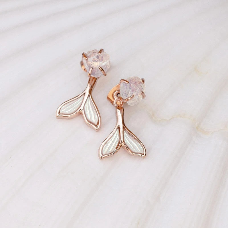 Rose gold mermaid tail earrings with clear gemstones on a marble background