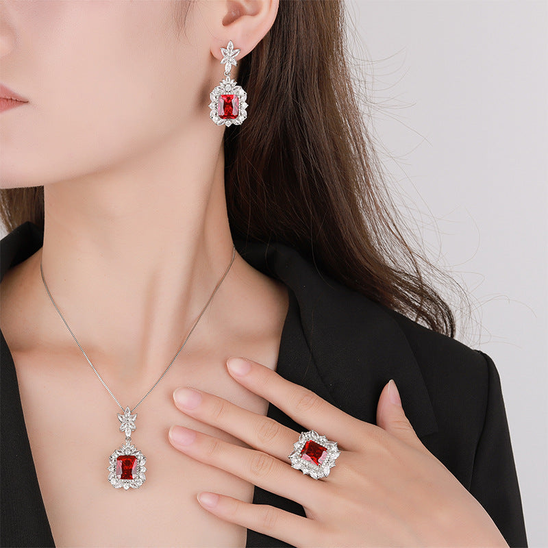 Red gemstone jewelry set including earrings, necklace, and ring on a model against a neutral background