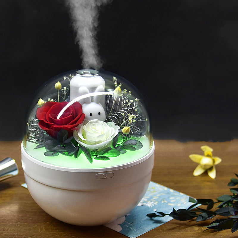 Humidifier with decorative flowers inside a glass dome on a wooden surface.
