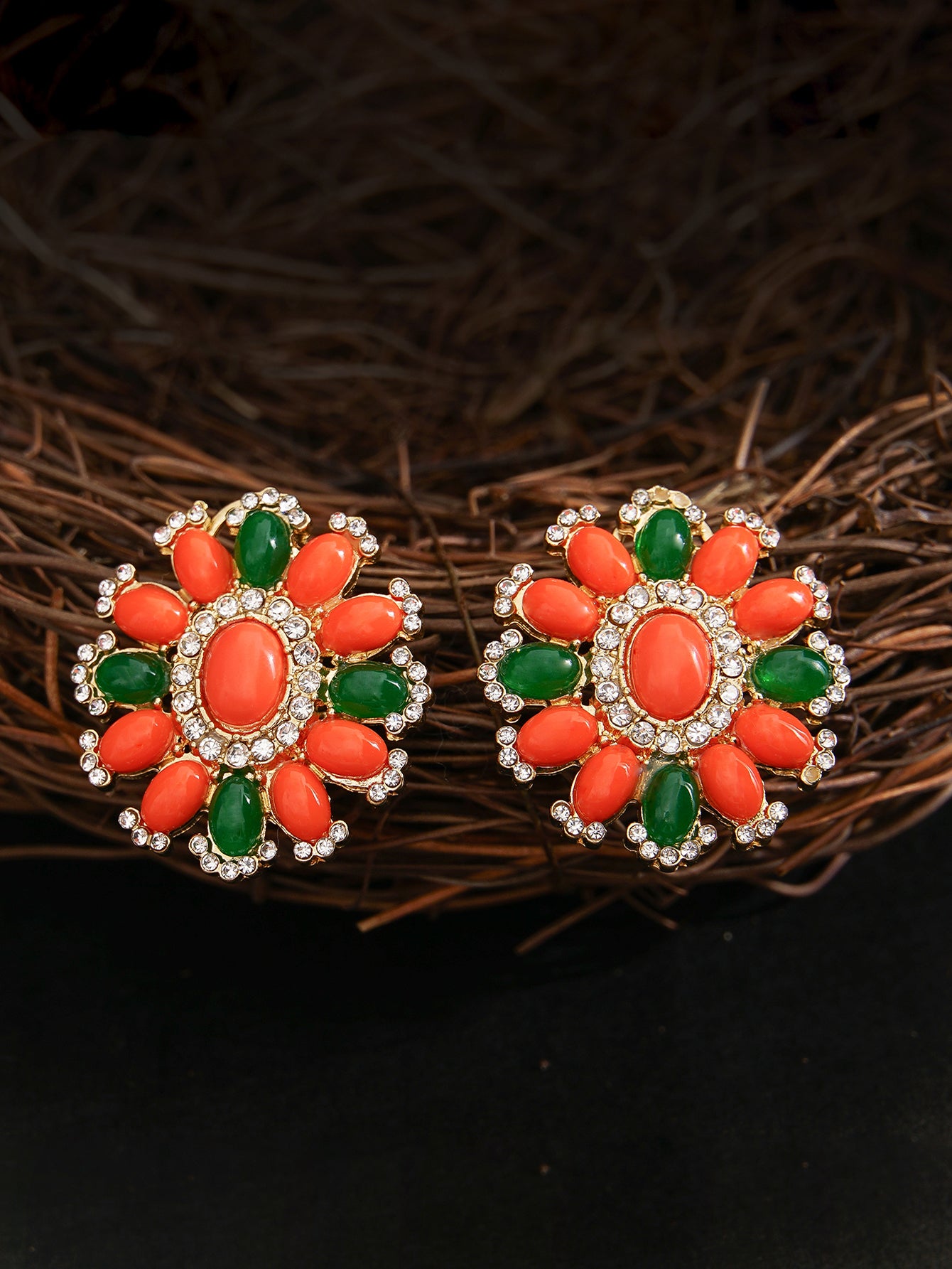 Pair of floral earrings with orange and green stones on a dark background