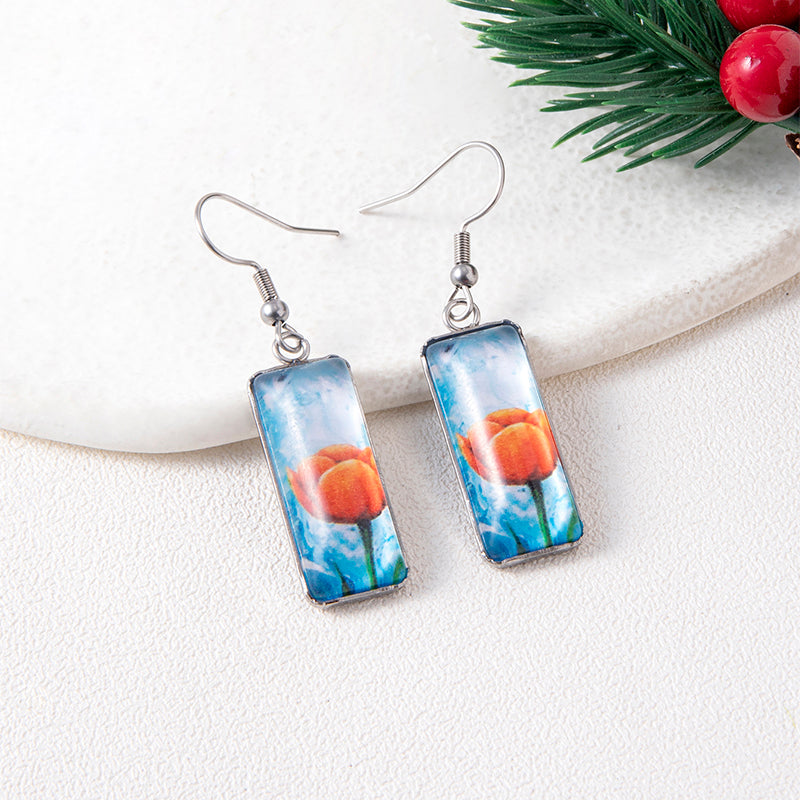 Rectangular earrings with peach design on a white surface with greenery.