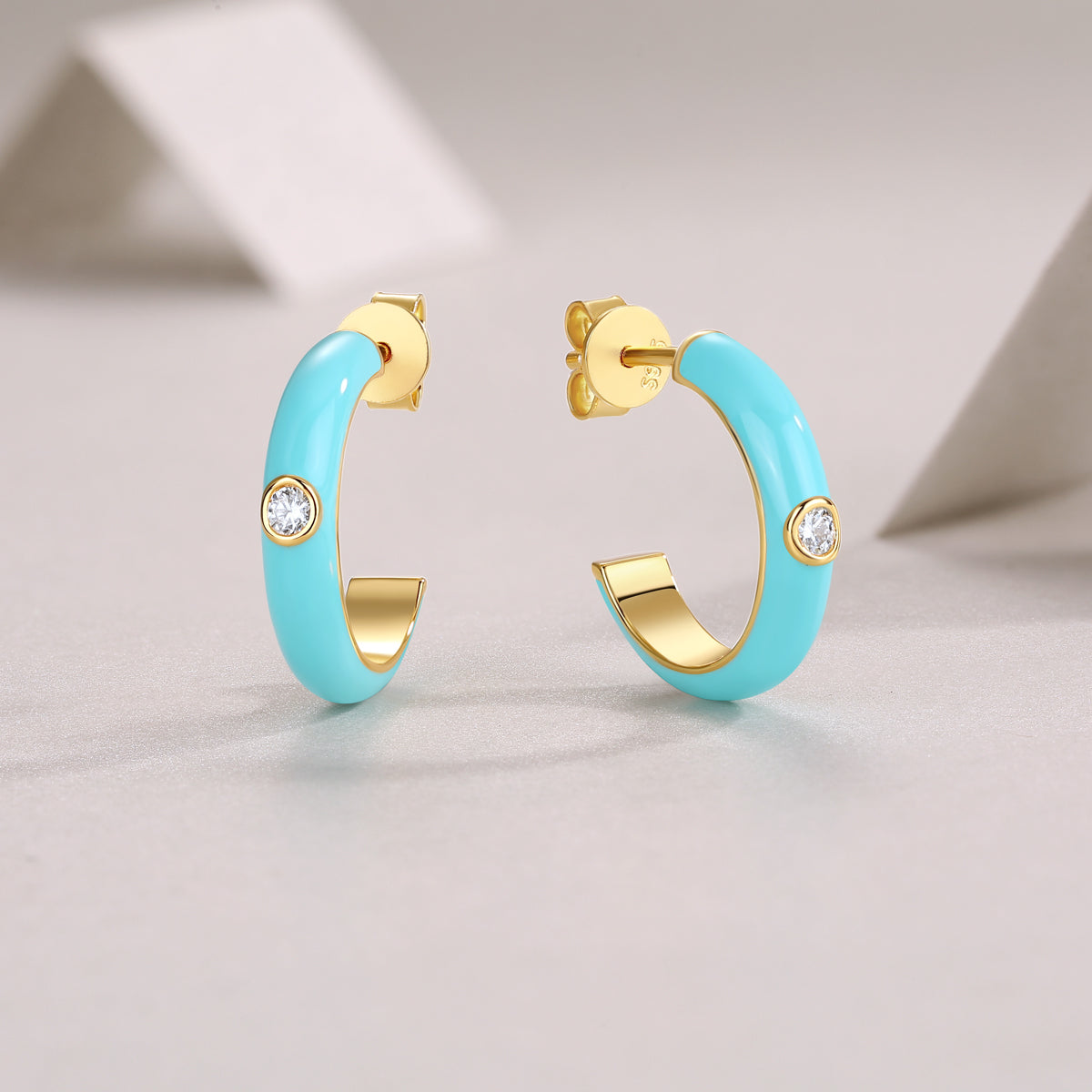 Turquoise hoop earrings with gold accents on a light gray background