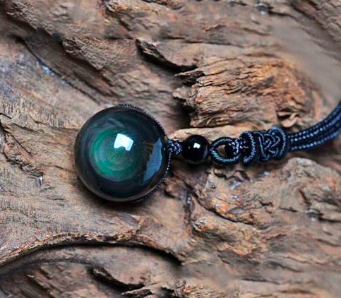 Black corded pendant with a green gemstone on a wooden surface