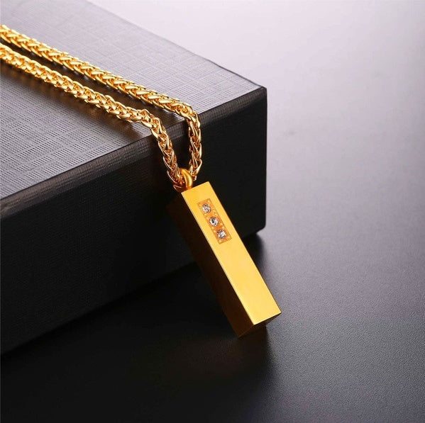 Gold necklace with a rectangular pendant on a dark surface