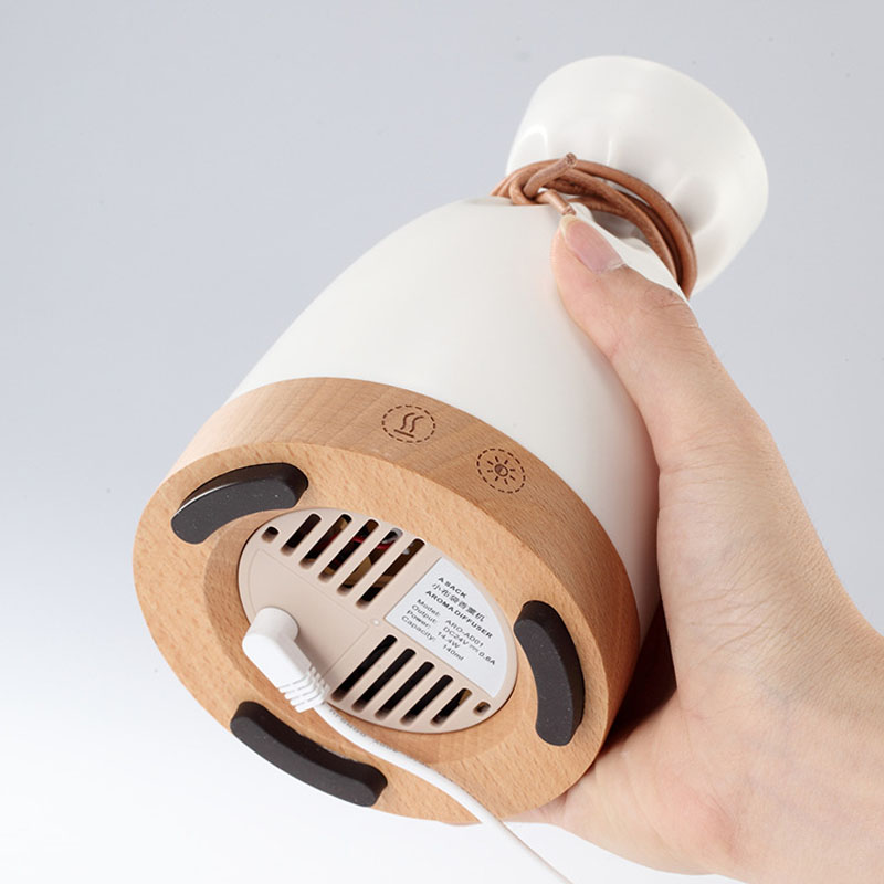 Hand holding a white and wooden device with a cable on a light gray background