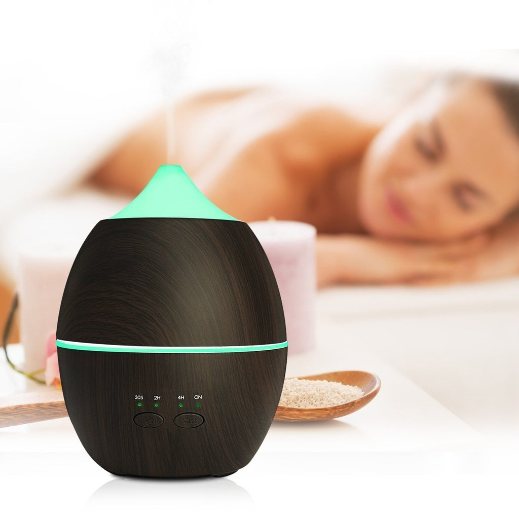 Black essential oil diffuser with green accents on a blurred background of a person relaxing.