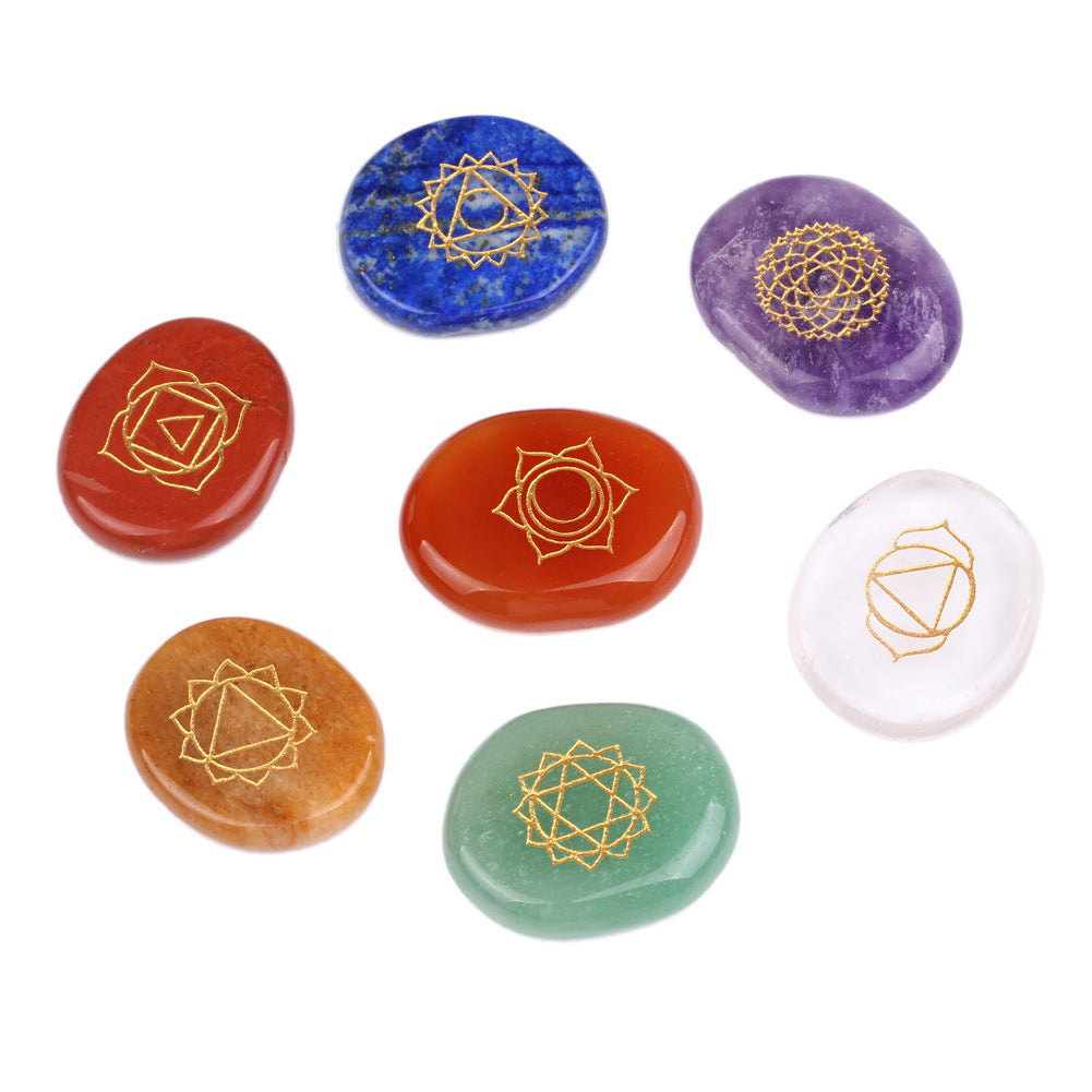 Set of seven chakra stones with gold geometric designs on a white background