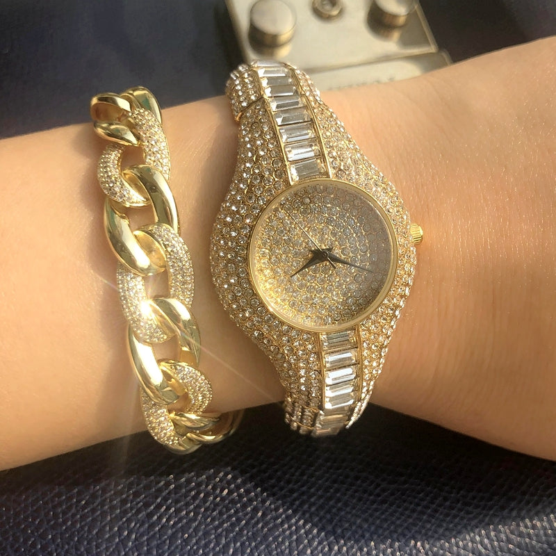Gold watch and bracelet on a wrist against a dark background
