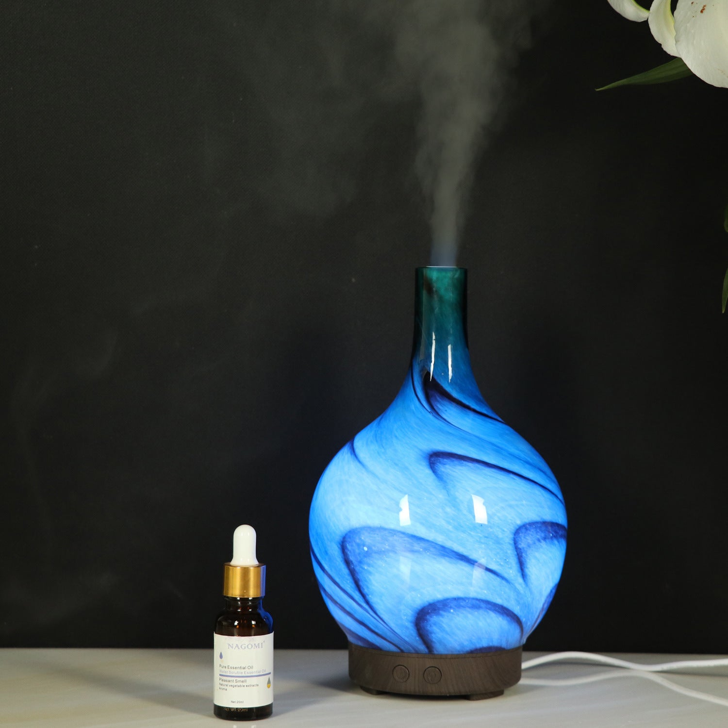 Blue diffuser emitting steam with a dropper bottle on a dark background