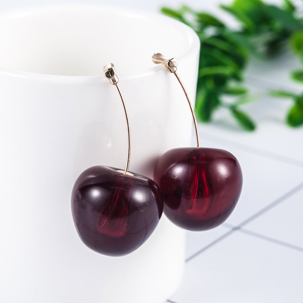 Cherry-shaped earrings on a white background with green leaves.