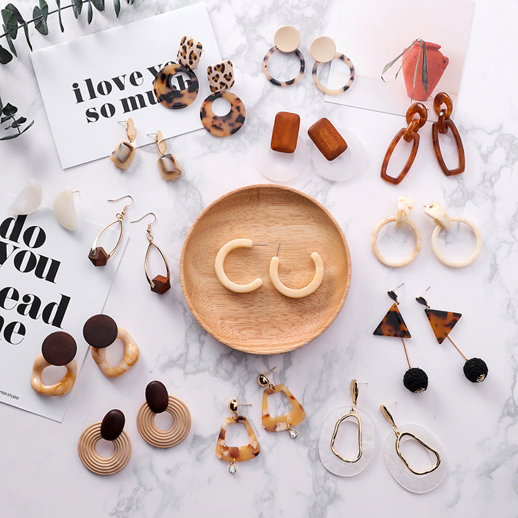 Collection of various earrings on a marble surface with a wooden plate.