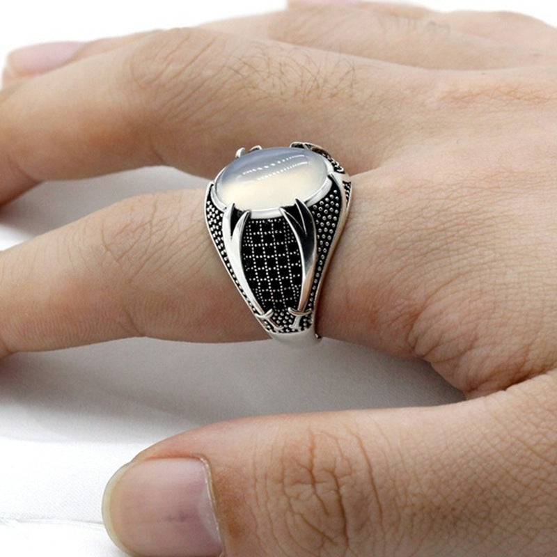Silver ring with black pattern on a finger against a white background