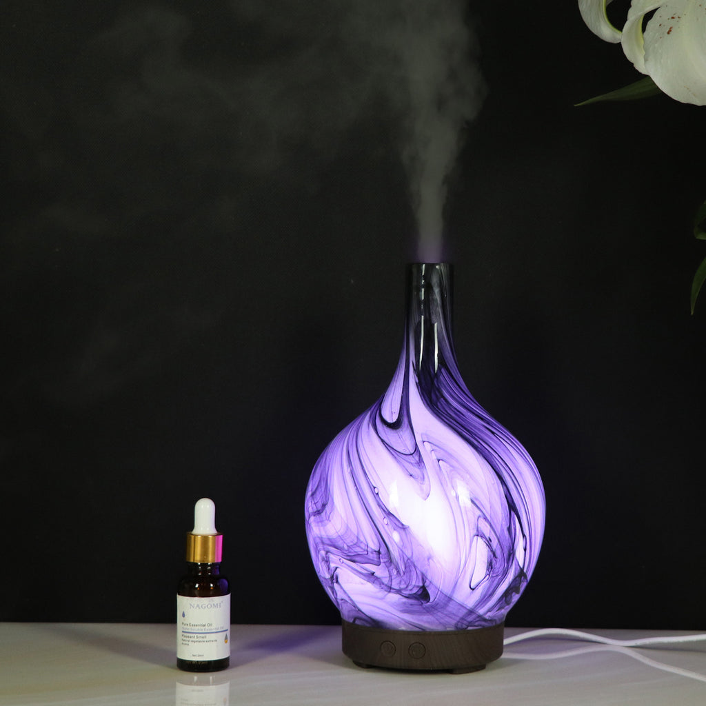 Purple marbled diffuser emitting steam next to a small bottle on a dark background