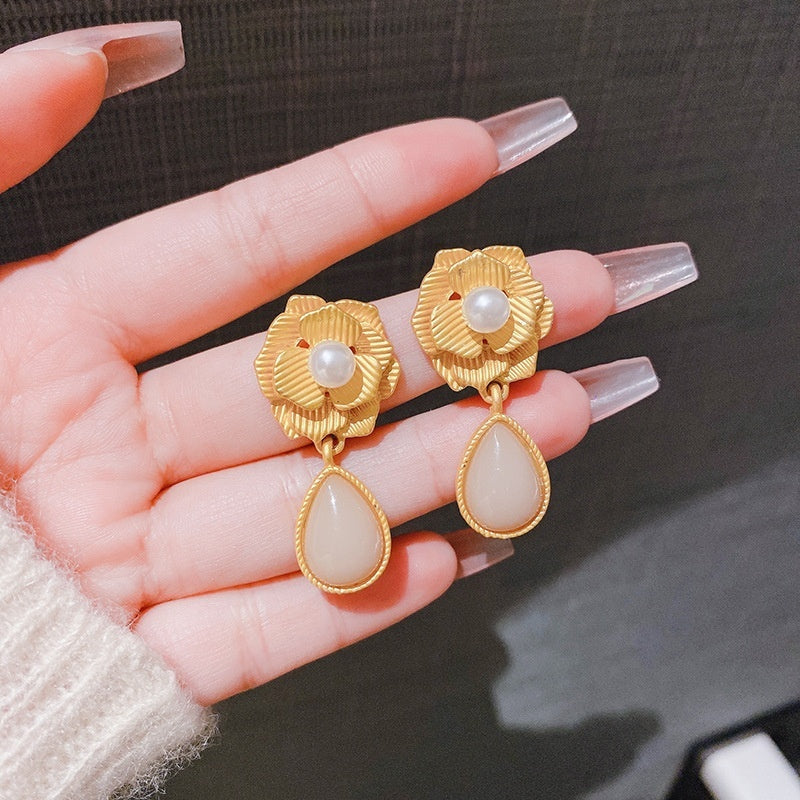 Gold earrings with pearl and stone details held in a hand against a dark background