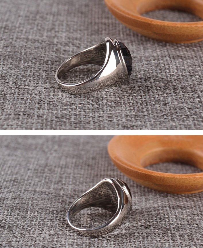 Silver ring with a black stone on a textured gray surface with wooden object in the background.