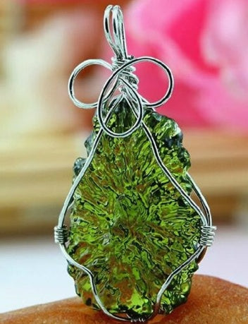 Green stone pendant with silver wire wrapping on a wooden surface