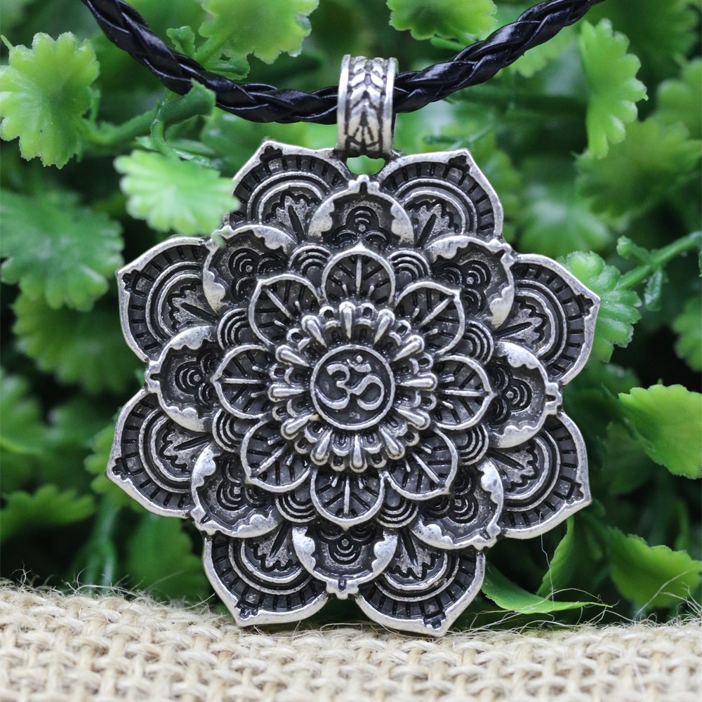 Silver mandala pendant with 'Om' symbol on a black cord against a green leafy background