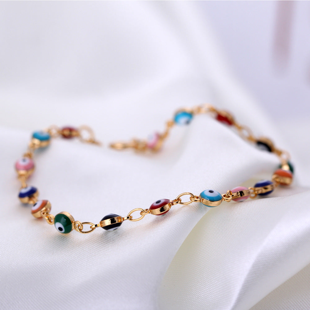 Colorful beaded bracelet with gold chain on a white fabric background