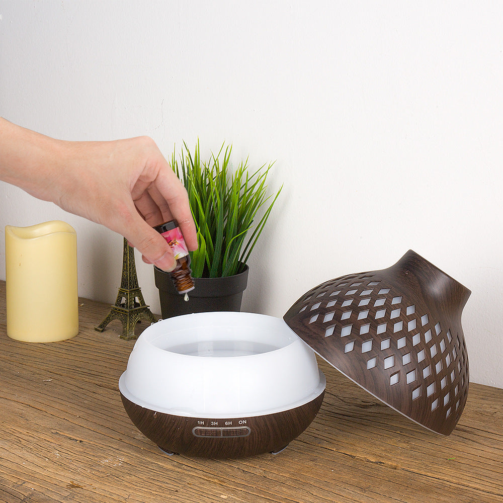 Hand adding essential oil to a diffuser with a plant and candle in the background
