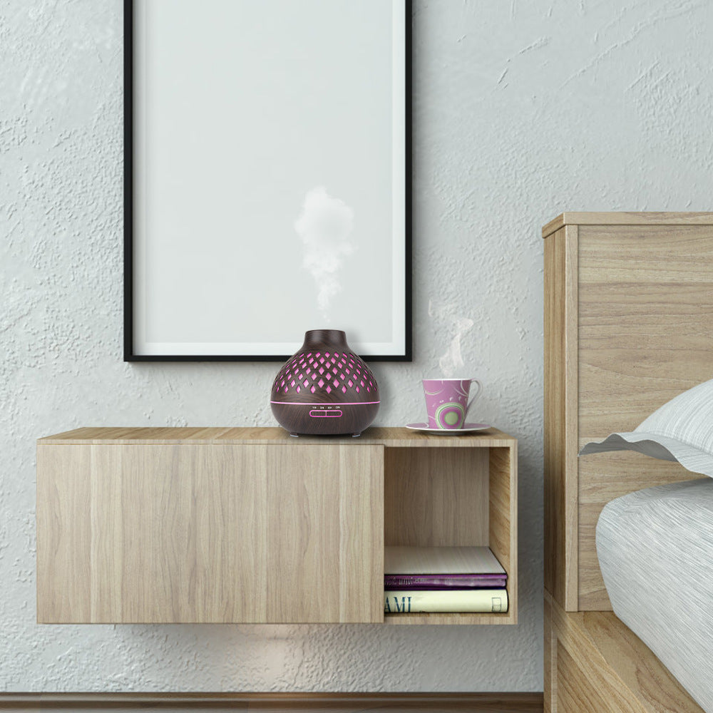 Wooden nightstand with pink diffuser and books next to a bed with white bedding.