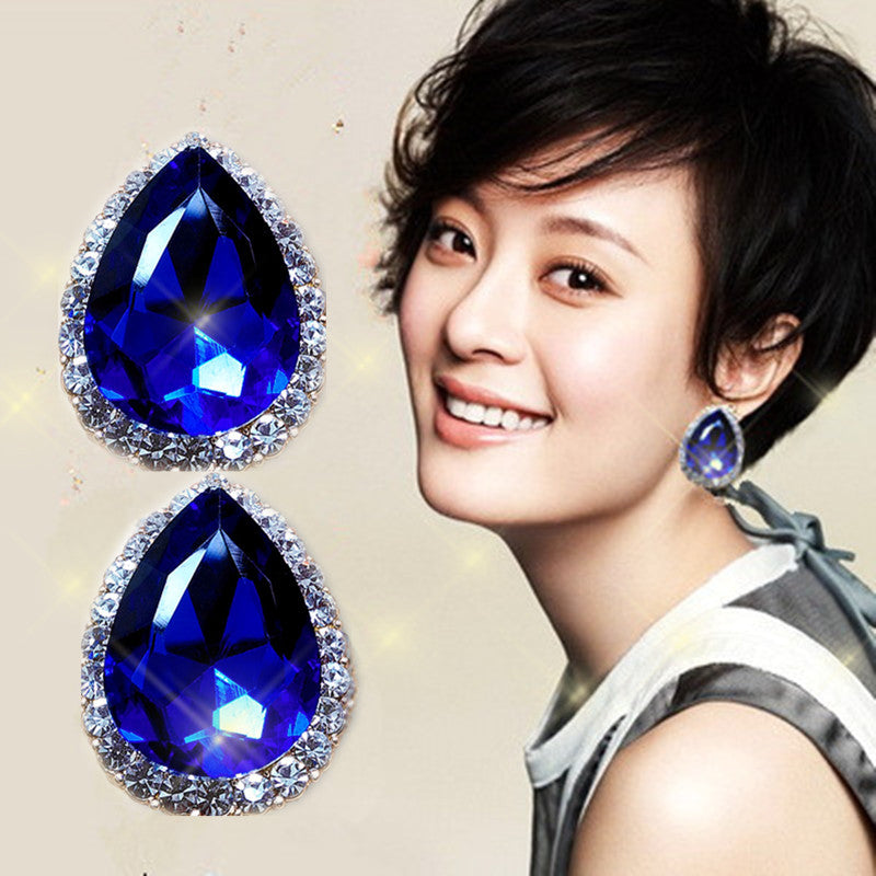 Woman wearing blue teardrop earrings with a beige background