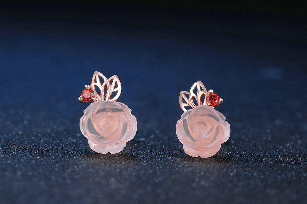 Pair of floral earrings with pink flowers and red gemstones on a dark background
