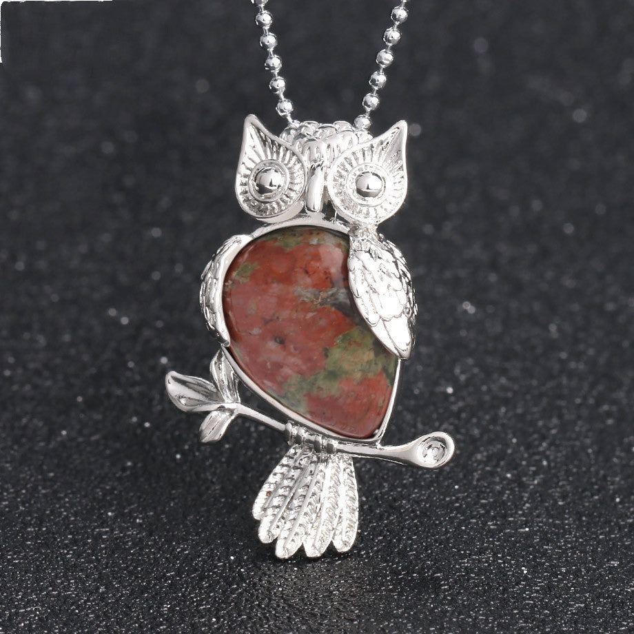 Silver owl-shaped pendant with a red stone on a black background