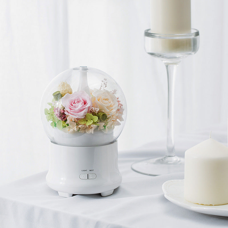 Small round white lamp with a glass cover containing flowers on a white surface.