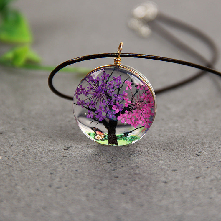 Necklace with a round pendant featuring a tree with purple and pink flowers on a gray surface.