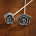 Two gray rose-shaped candles on wooden sticks against a wooden background
