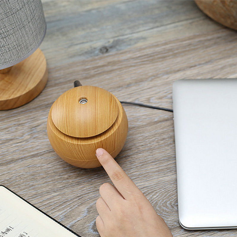 Wooden diffuser on a wooden surface with a hand pointing at it